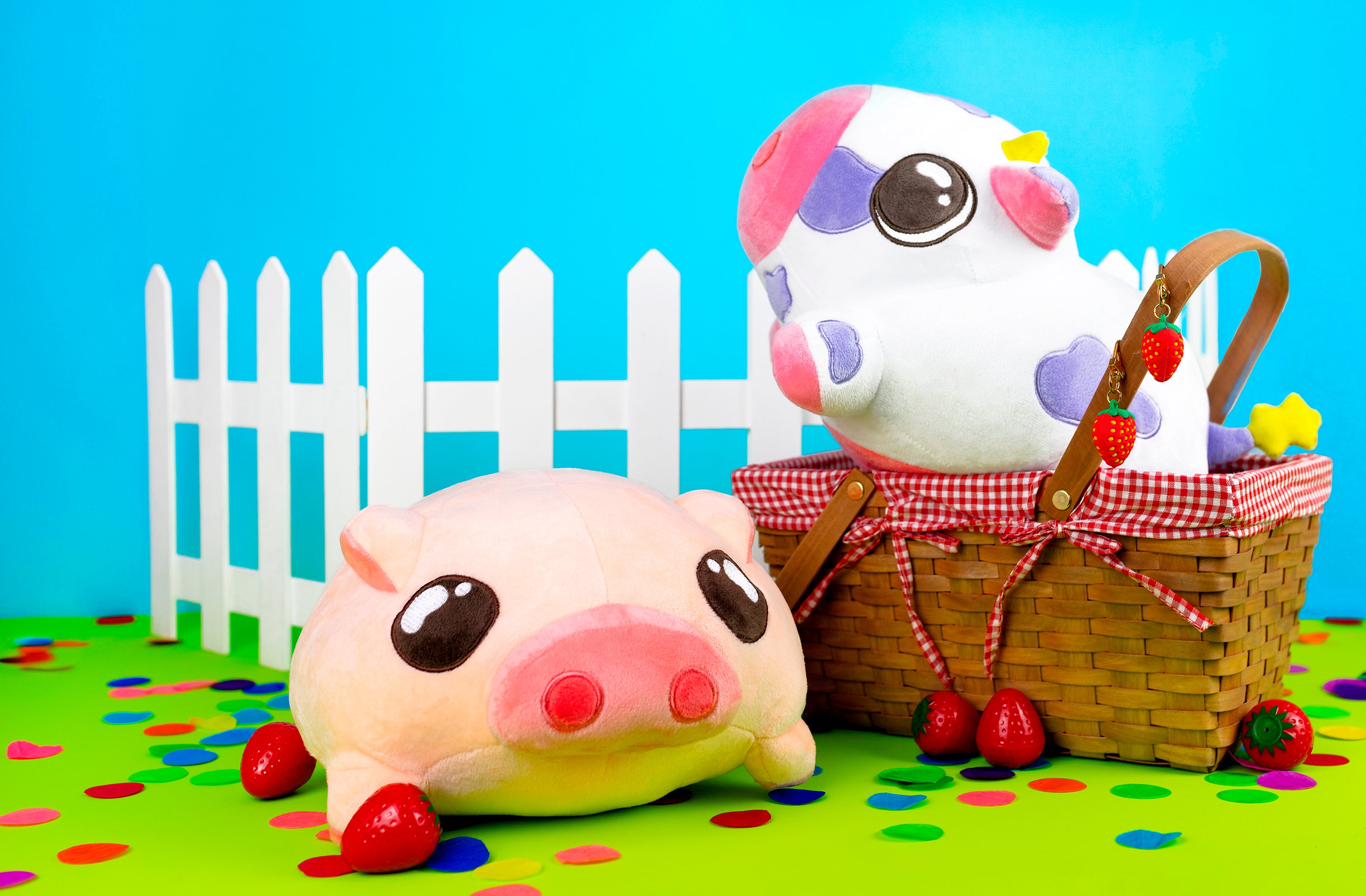 Cow plushie and piggy plushie in front of a white fence and picnic basket